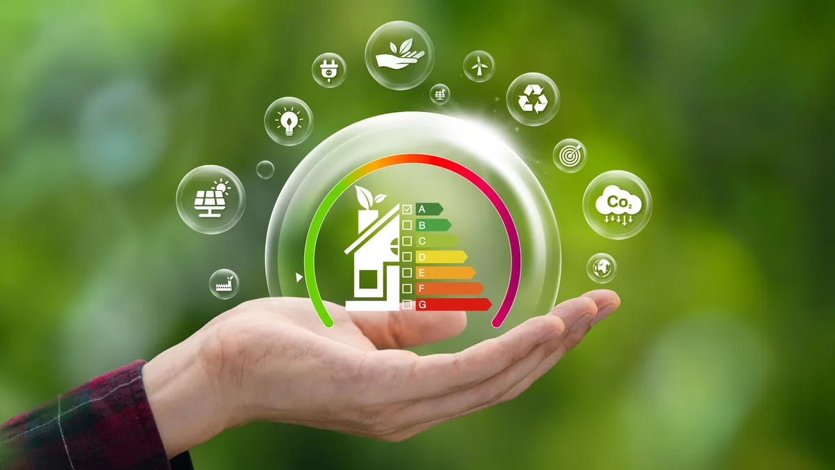 Hand hält eine Glasblase mit Haus und Energieeffizienzskala, umgeben von Symbolen für Photovoltaik, Windkraft und CO2