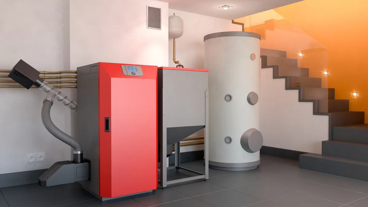 Roter Pelletkessel mit Vorratsbehälter neben einem großen Warmwasserspeicher in einem hellen Heizungsraum